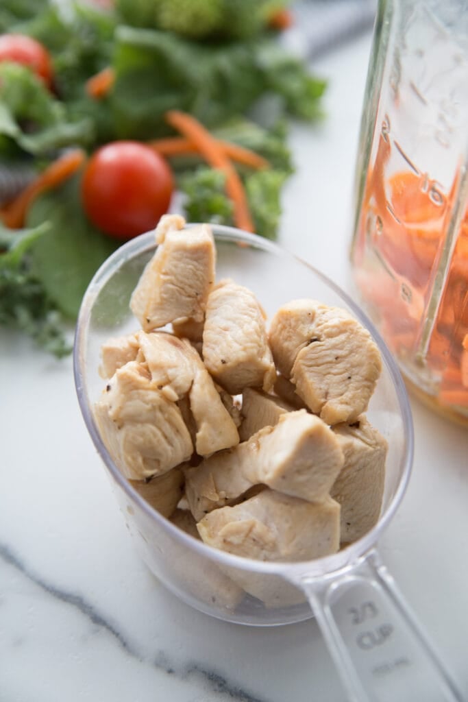 A cup of chicken next to a mason jar getting ready for mason jar salad assembly 