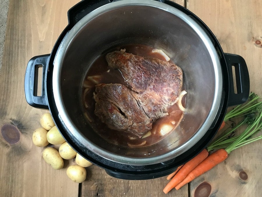 A photo of an open Instant Pot with a roast at the bottom next to some carrots and potatoes