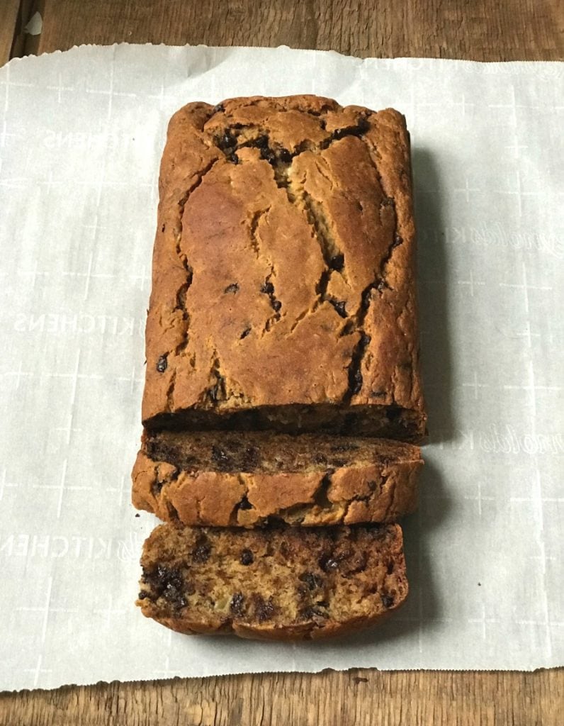 Overhead photo of a loaf of healthy banana bread with chocolate chips cut into a couple slices, on a parchment lined wooden cutting board.