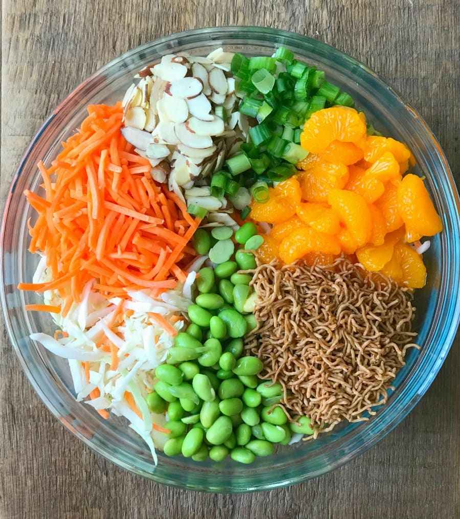 Glass bowl filled with Salad- Cabbage, Carrots, Almond, Green Onions, Mandarin Oranges, and toasted brown rice ramen noodles.