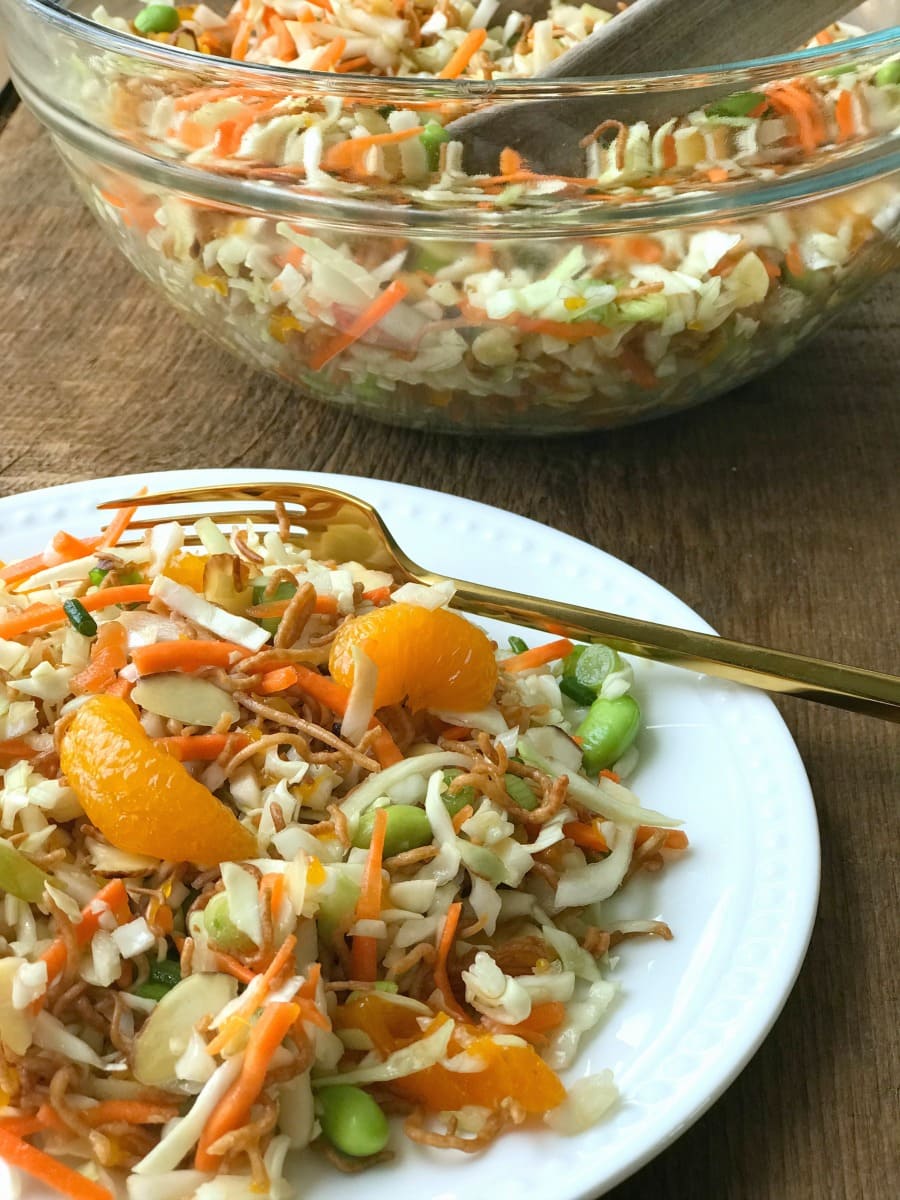 A small white plate of Ramen Noodle Salad next to a large glass bowl of Ramen Noodle Salad in the background