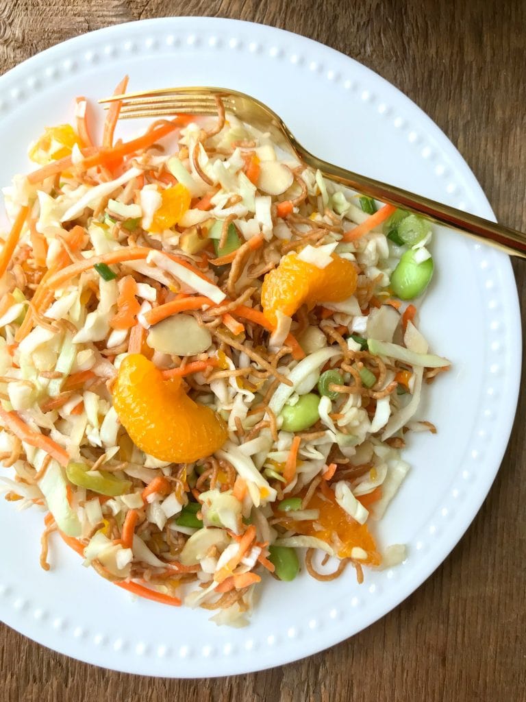 White plate with crunchy ramen salad topped with oranges