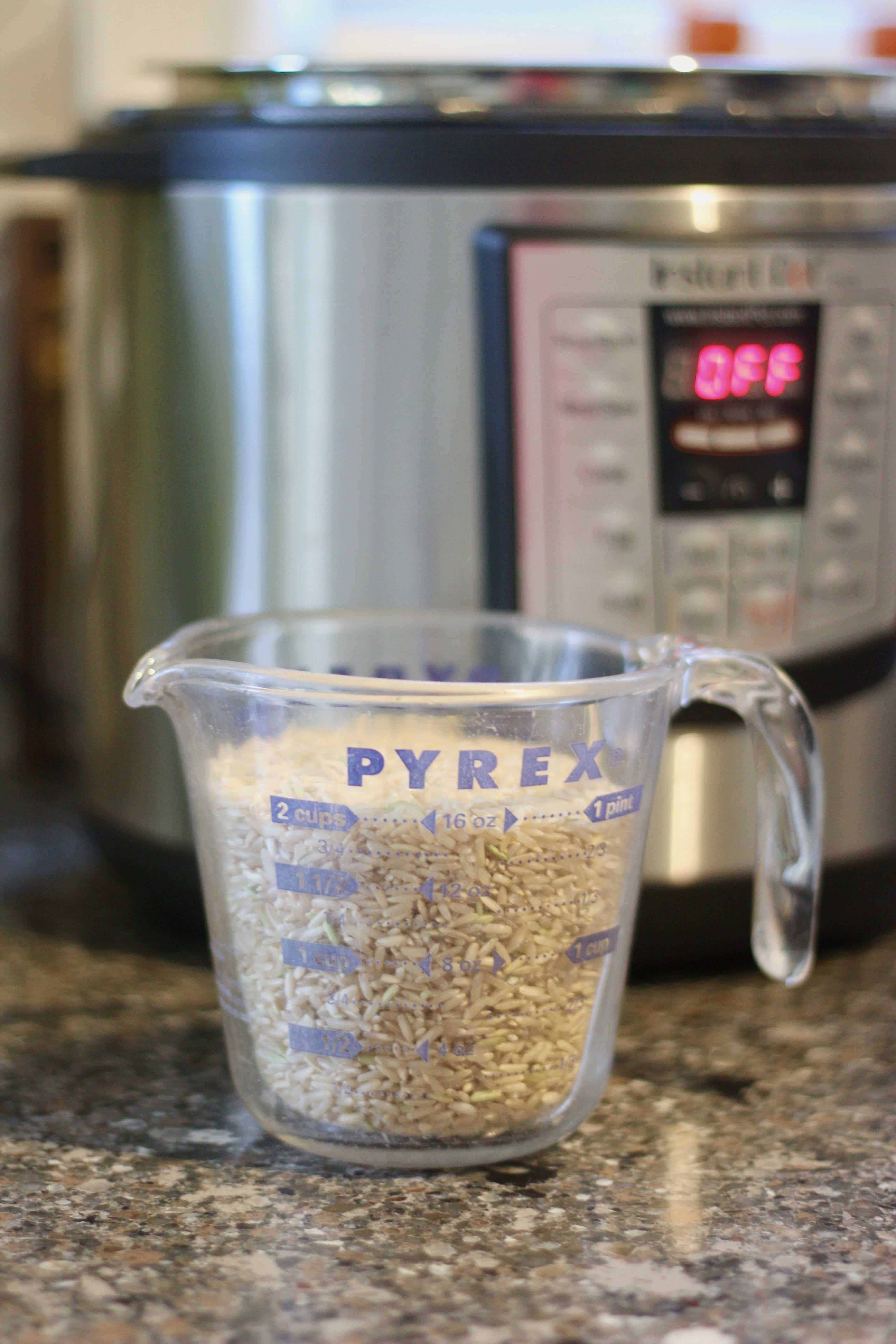 Measuring cup full of brown rice with an Instant Pot in the background