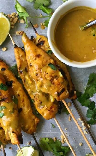 Chicken Satay Skewers on a Baking Pan with Creamy peanut sauce, crushed peanuts, and lime wedges