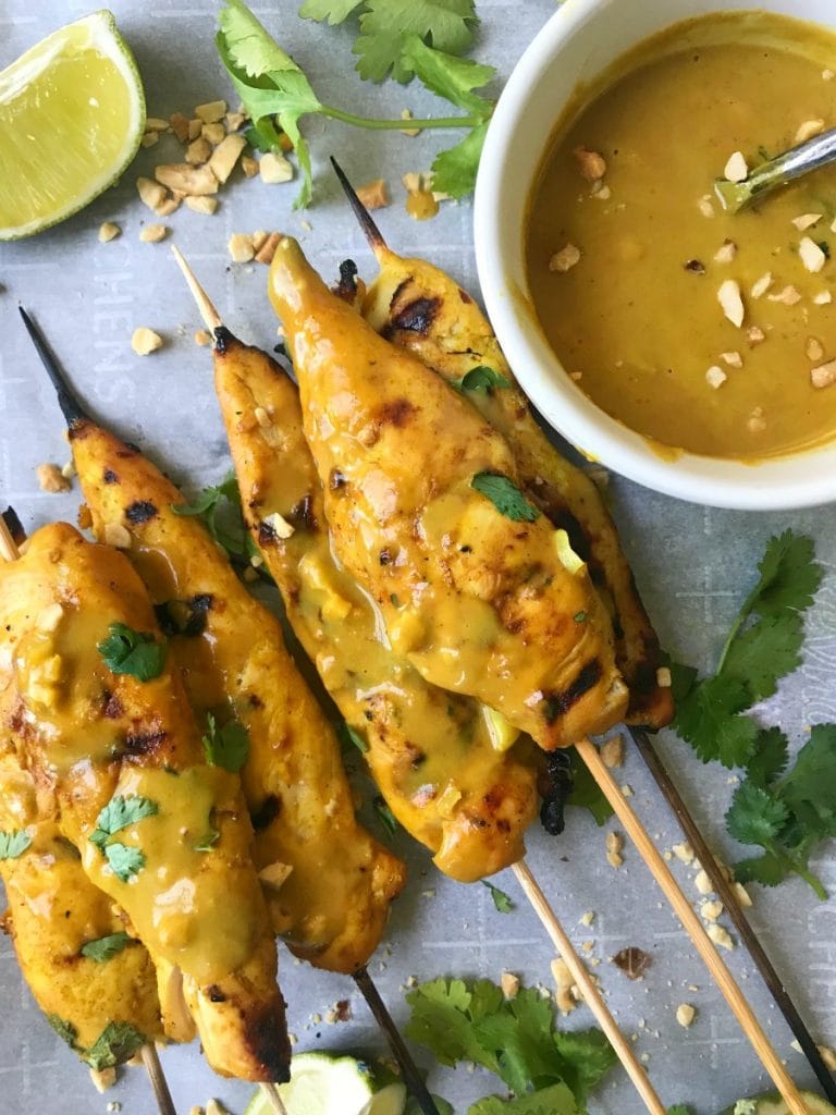 Chicken Satay Skewers on a Baking Pan with Creamy peanut sauce, crushed peanuts, and lime wedges