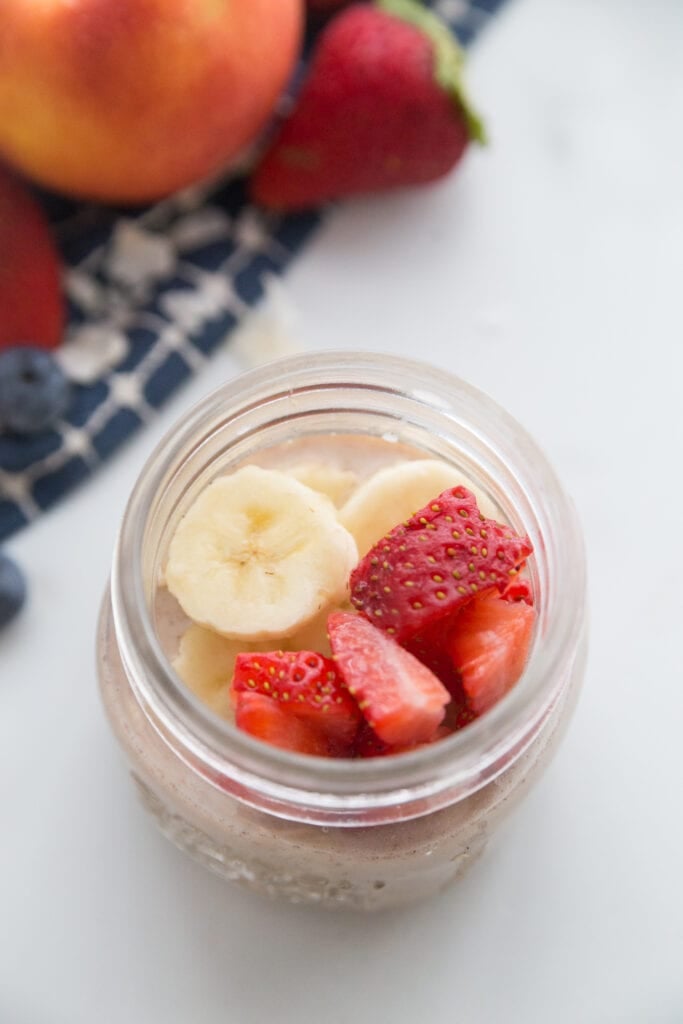 Strawberry banana overnight oats sitting next to a blue napkin with fruit on top 