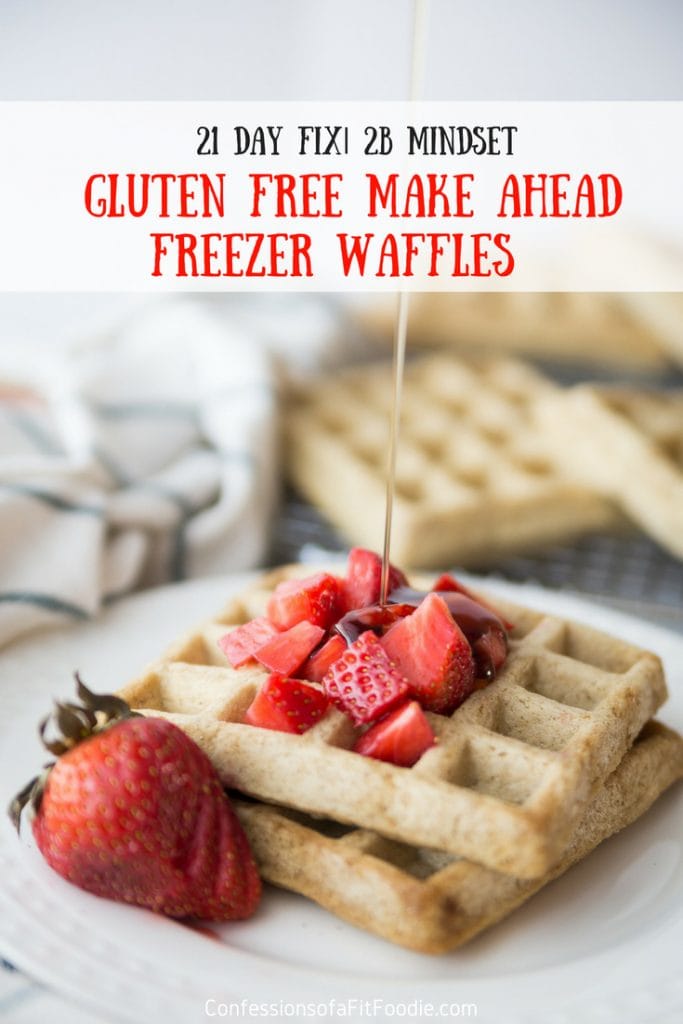 Two square homemade waffles on a white plate topped with diced strawberries and a sliced strawberry for garnish. Maple syrup is being drizzled from above. Has the text overlay- 21 Day Fix | 2B Mindset Gluten Free Make Ahead Freezer Waffles