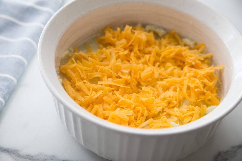 A white Instant Pot safe casserole dish with cauliflower mash topped with freshly shredded cheese