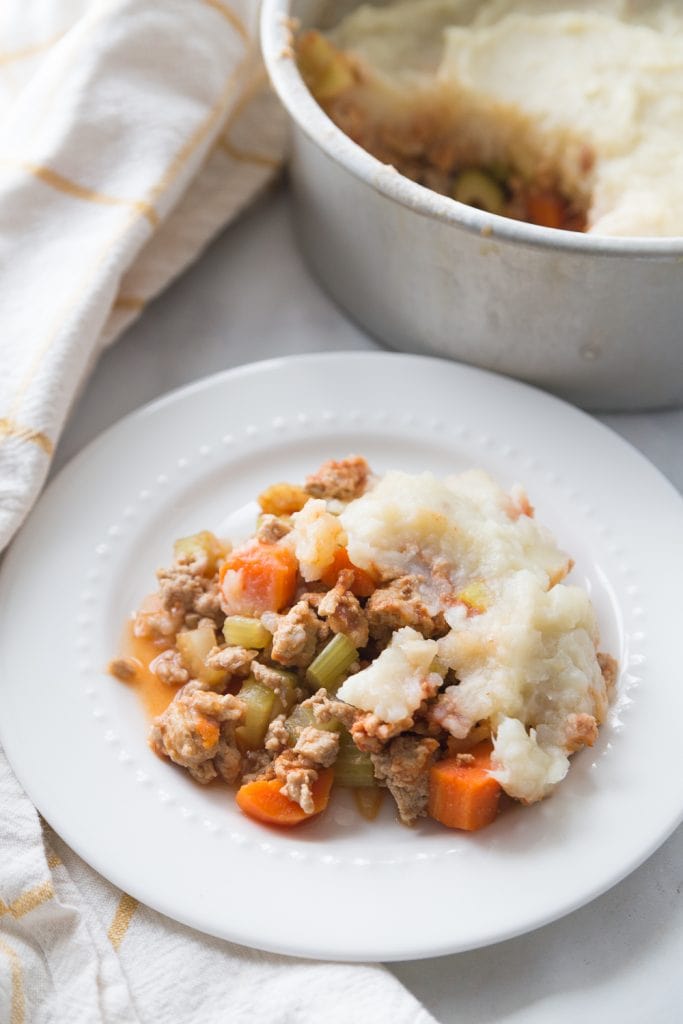 Healthy Shepherd's Pie on a white plate with a circular metal dish in the background