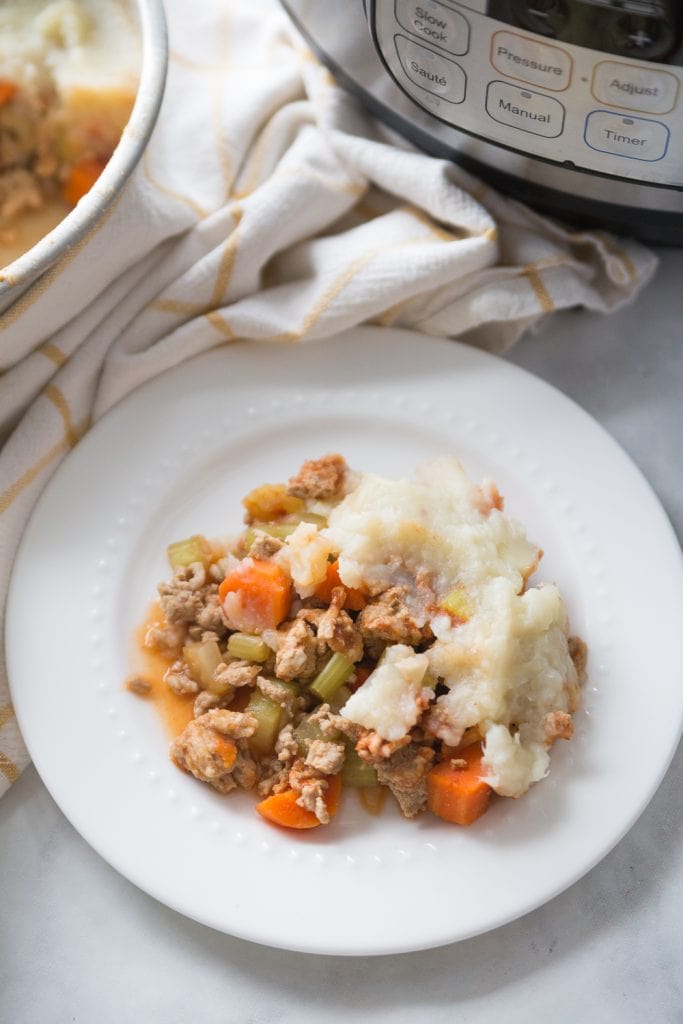 White plate with healthy shepherd's pie topped with mashed cauliflower and mashed potatoes sitting near an Instant Pot