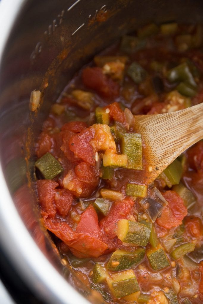 Cooked ratatouille in the instant pot being stirred by a wooden spoon