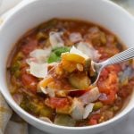 White bowl with warm ratatouille , topped with parmesan and fresh basil