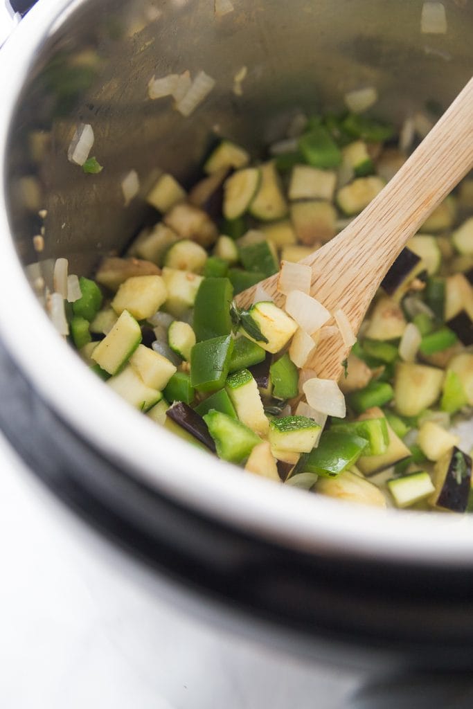 Chopped zucchini, peppers, and onions being cooked in the Instant Pot with a wooden spoon resting on the side