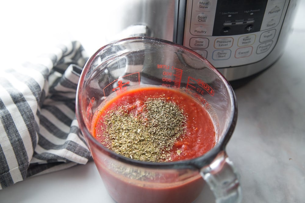 A measuring cup of sauce and spices next to an Instant Pot