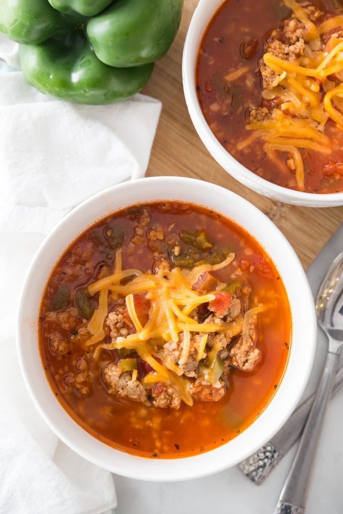 Two white porcelain bowls with low carb stuffed pepper soup topped with shredded cheddar cheese.