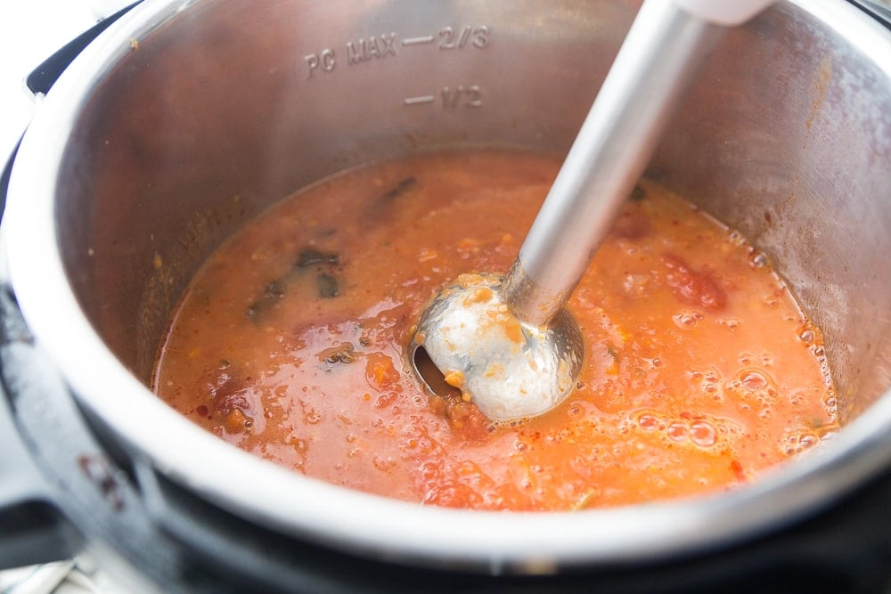 Instant Pot tomato soup being blended using a stainless immersion blender 