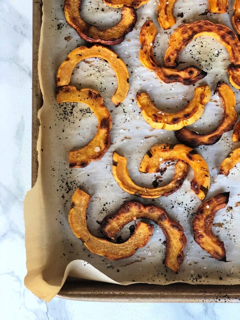 Roasted delicata squash on a baking sheet. Edges are crispy and the fries are seasoned. 