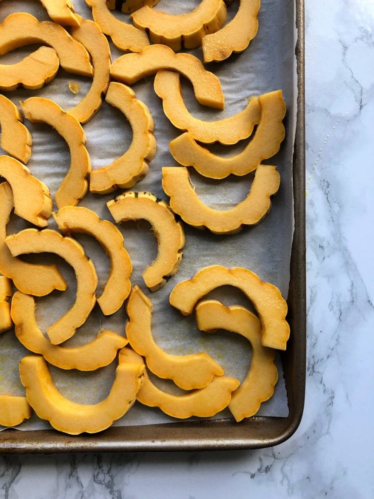 Sliced delicata squash on a rimmed baking sheet over parchment paper