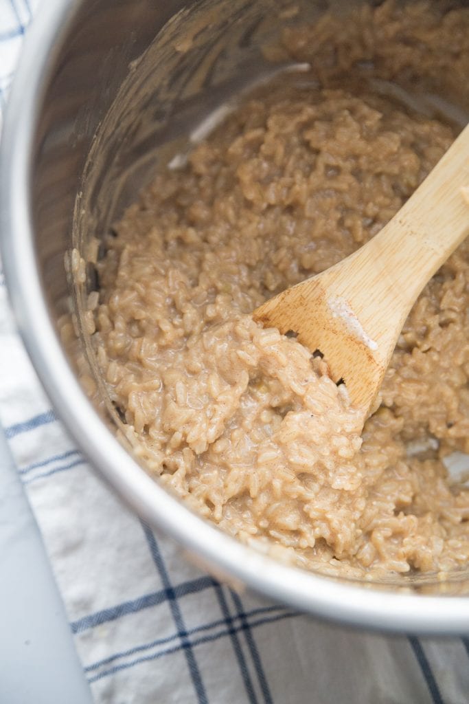 The inner lining of an instant pot with creamy delicious brown rice pudding being stirred with a wooden spoon.