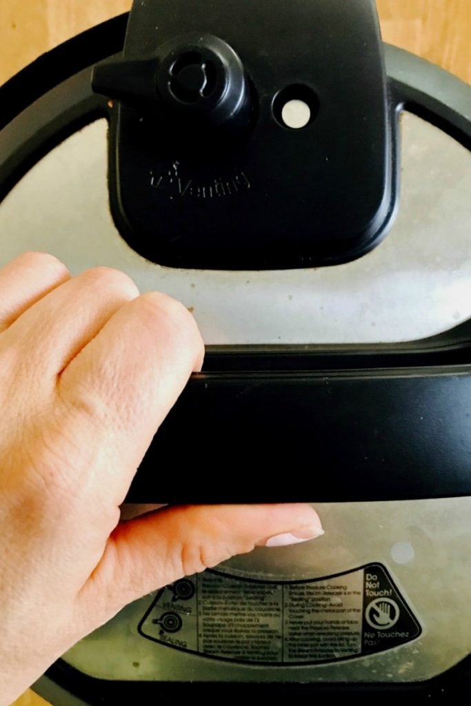 Overhead photo of Woman's hand resting on top of Instant Pot handle, ready to turn it.