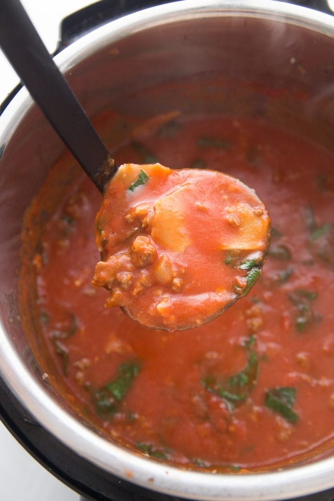 An overhead photo of an Instant Pot full of healthy instant pot lasagna soup. A ladle full of soup is in the foreground.