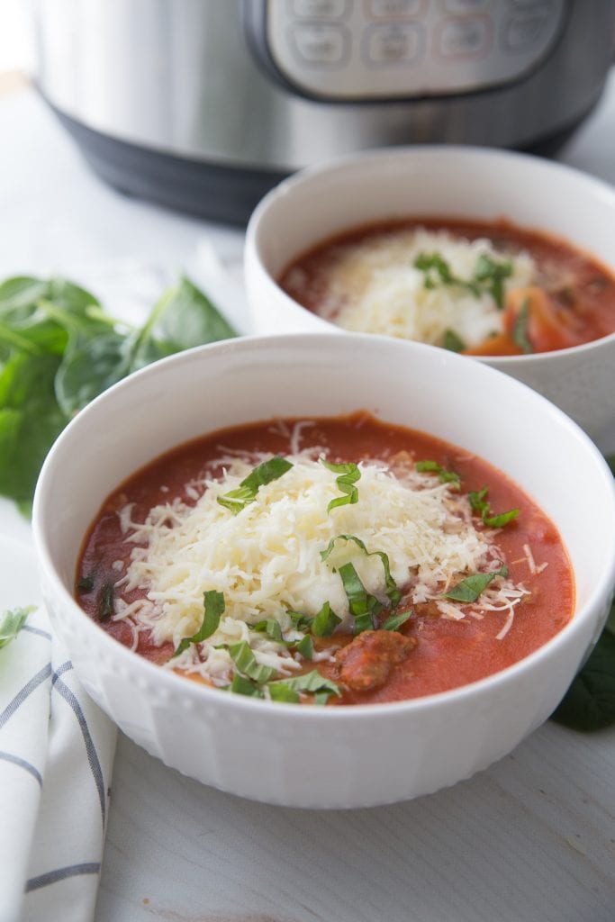 Two bowls of instant pot lasagna soup topped with cheese and fresh basil in front of an instant pot