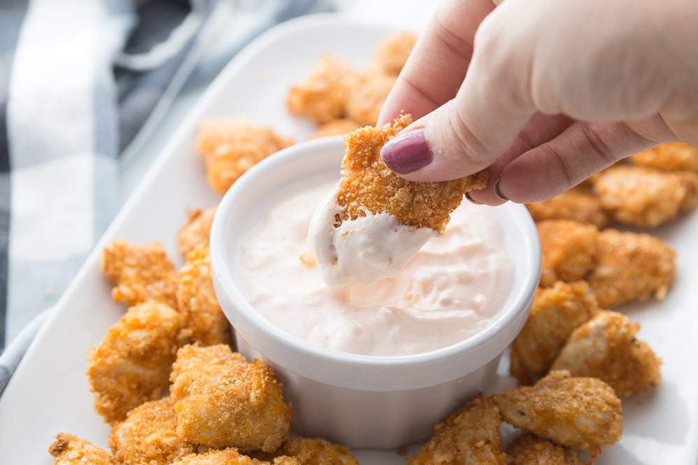 A platter of Air Fryer Buffalo Chicken Nuggets with one being dipped in buffalo blue cheese dip 