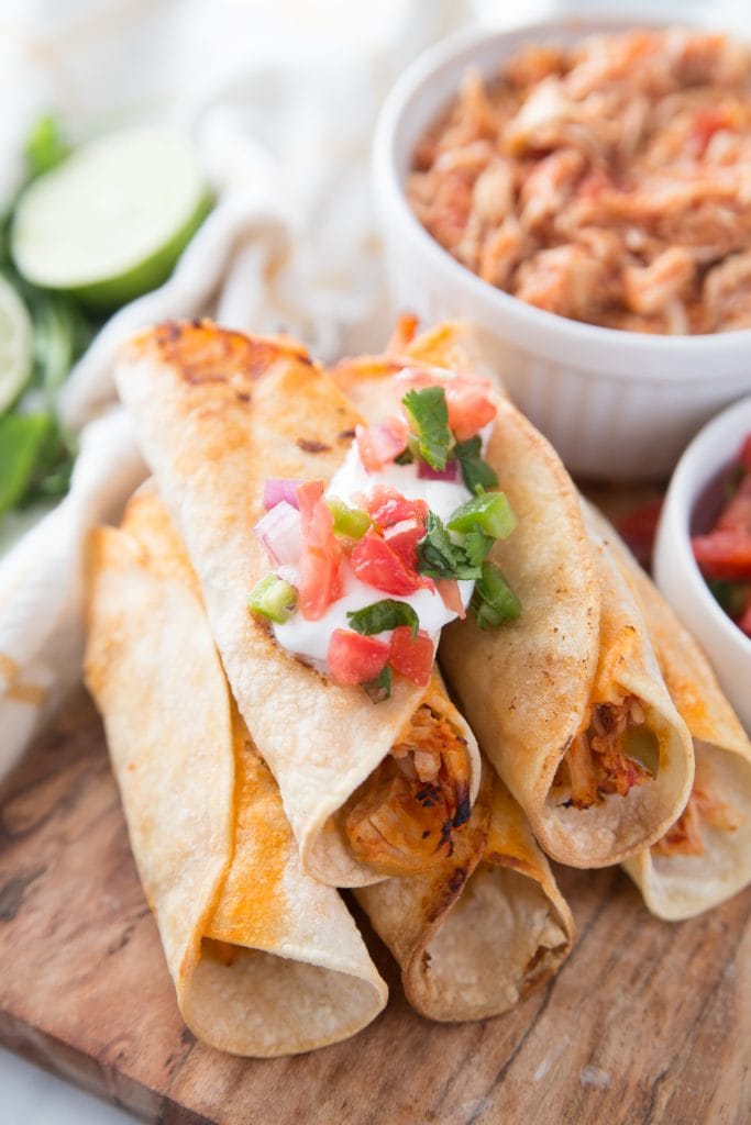 A pile of Chicken Taquitos on a wooden cutting board garnished with fresh salsa 