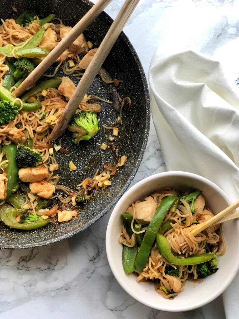 A small white bowl of 21 day Fix Chicken and Ramen Noodle Stir Fry sits next to the skillet that it was served from. 