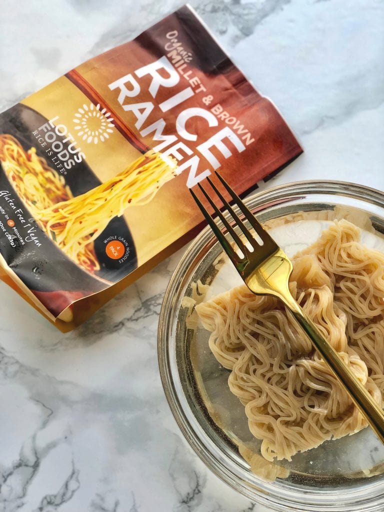 Lotus Foods Millet and Brown Rice Ramen in a bowl of water on a marble background.