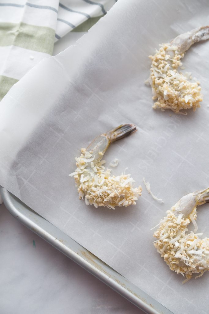uncooked gluten free coconut shrimp on a baking sheet lined with parchment paper 