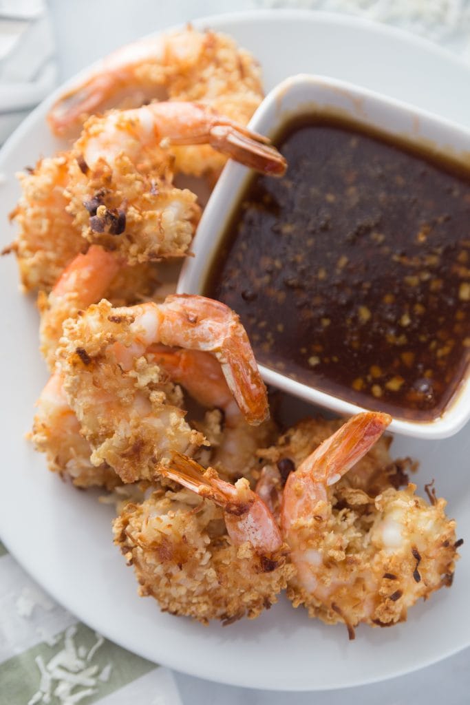 Overhead photo of Air Fryer Coconut Shrimp on a white plate with a side of sweet chili dipping sauce in a rectangular bowl