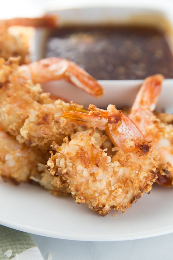 A close up shot of gluten free coconut shrimp with chili sauce in the background 
