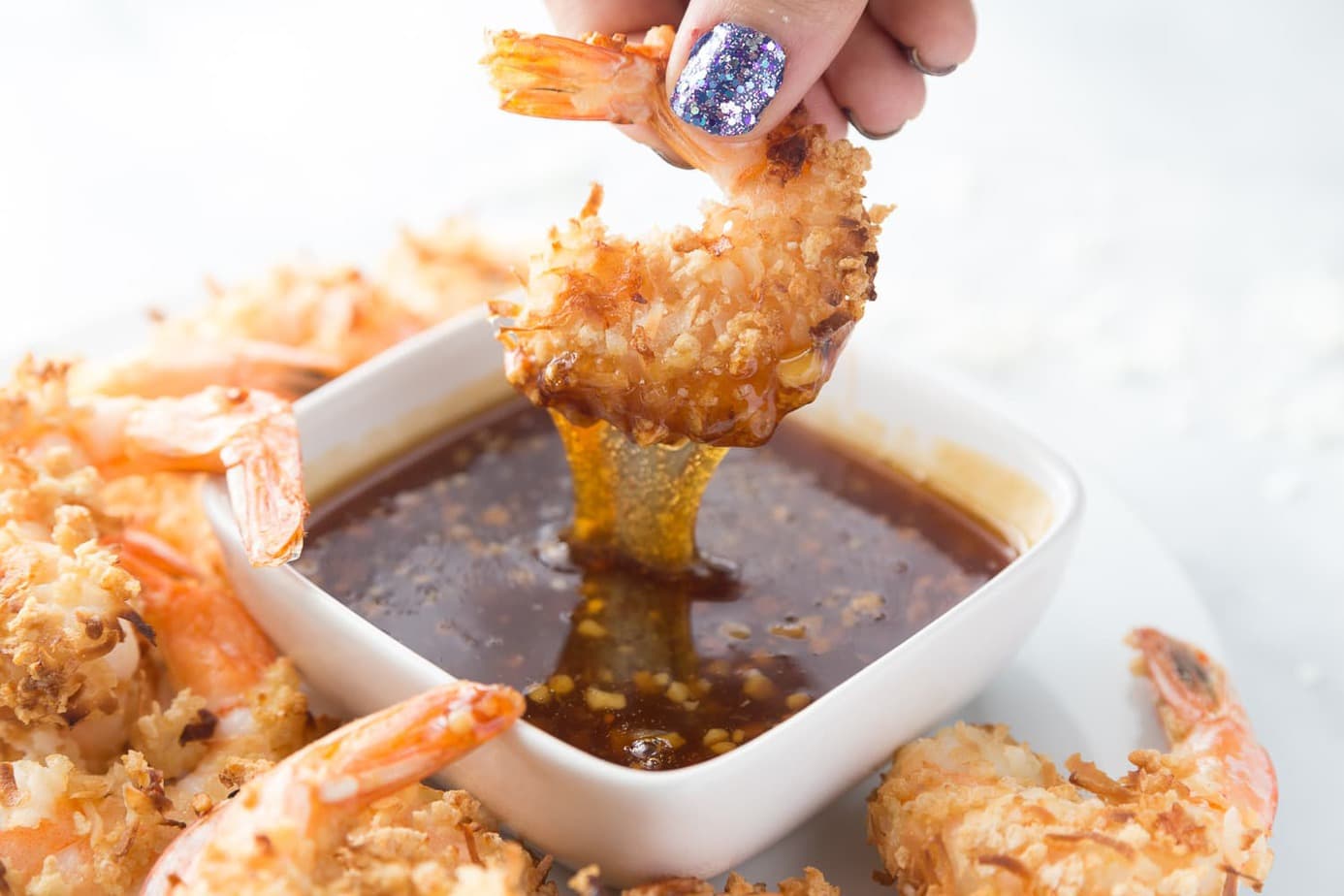 An air fried coconut shrimp is being dipped into some homemade thai sweet chili sauce
