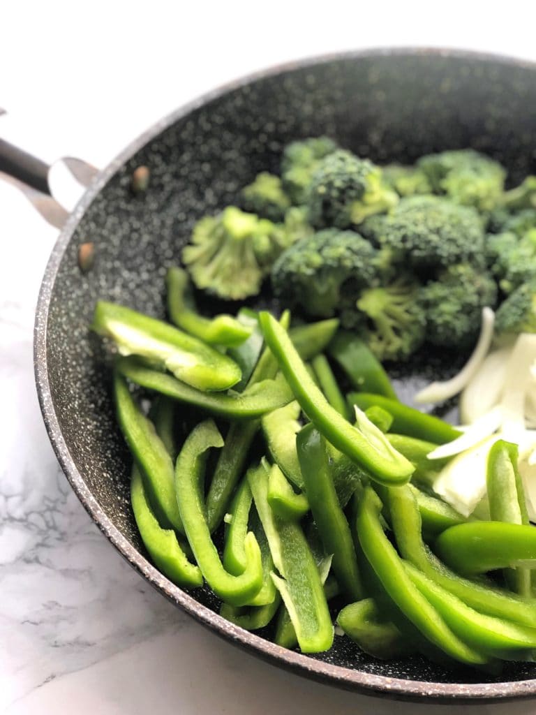 Skillet with bell peppers, broccoli and onions on a marble backdrop.