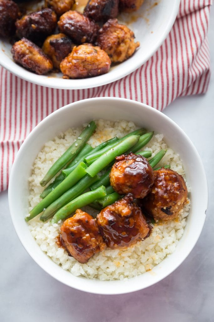 Asian Chicken Meatballs over Cauliflower Rice with Green Beans next to a bowl of meatballs