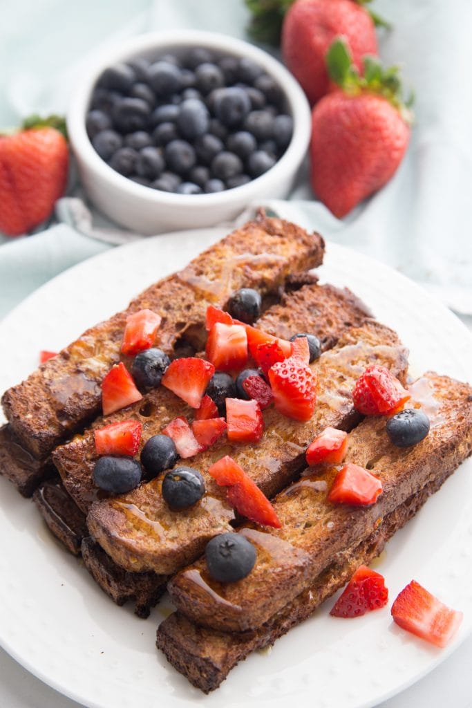 A stack of Healthy Air Fryer French Toast sits on a white plate and it's topped with strawberries and blueberries