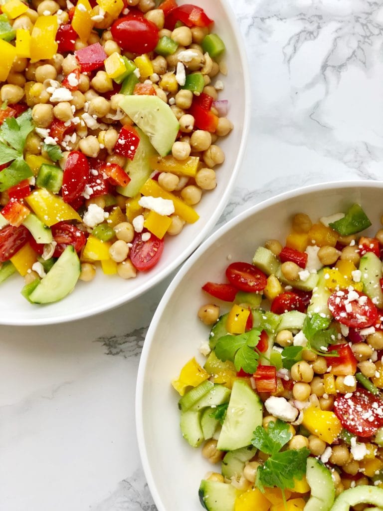 Two round white bowls of a colorful Mediterranean Chickpea Salad sitting on a marble backdrop. 