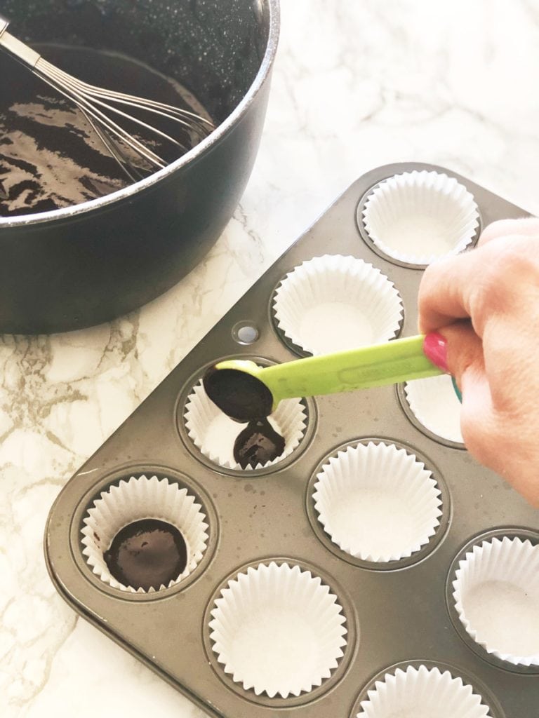 Filling a mini cupcake tin lined with paper liners with homemade chocolate for Reese's peanut butter cups 