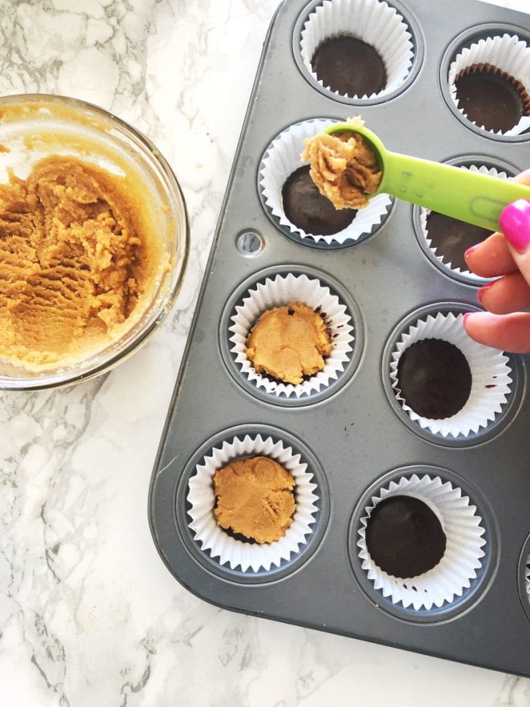 Making healthy mini copy cat peanut butter cups by layering a peanut butter mixture over some chocolate in a mini muffin tin
