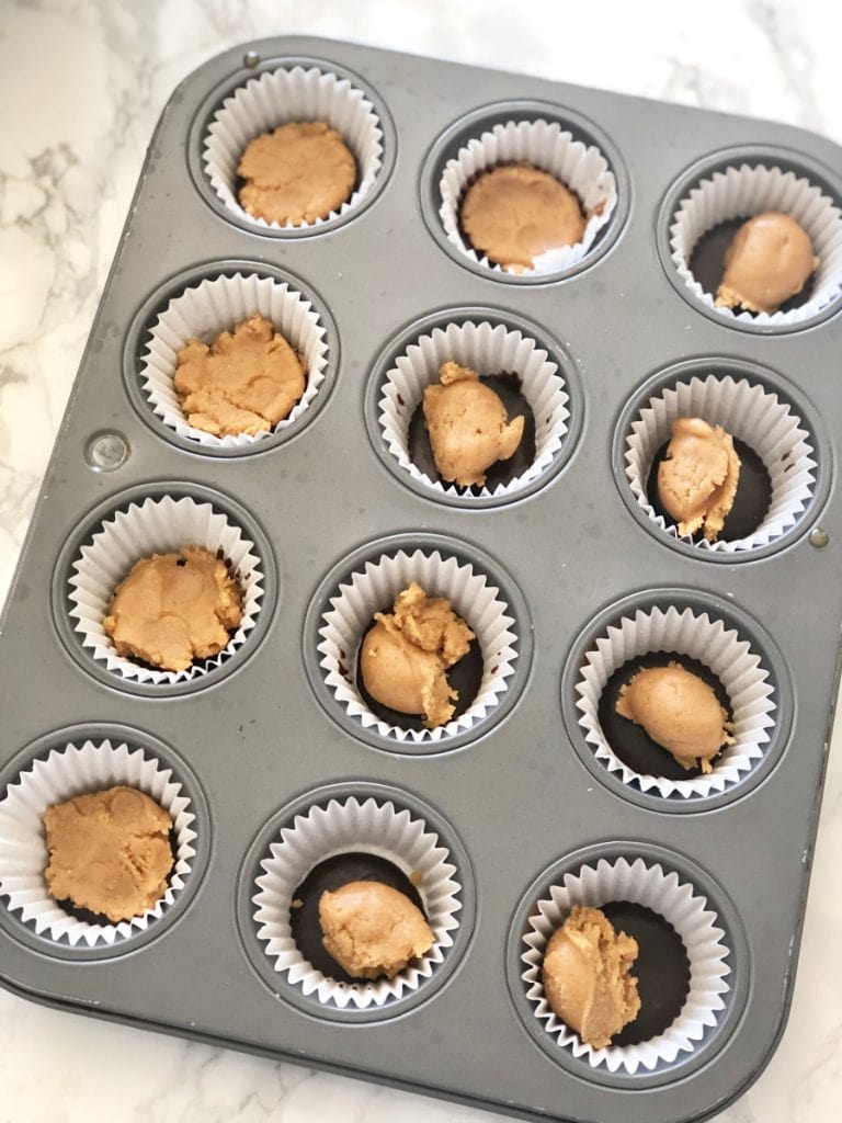 A mini cupcake tin lined with paper liners and a layer of chocolate and peanut butter for mini peanut butter cups 