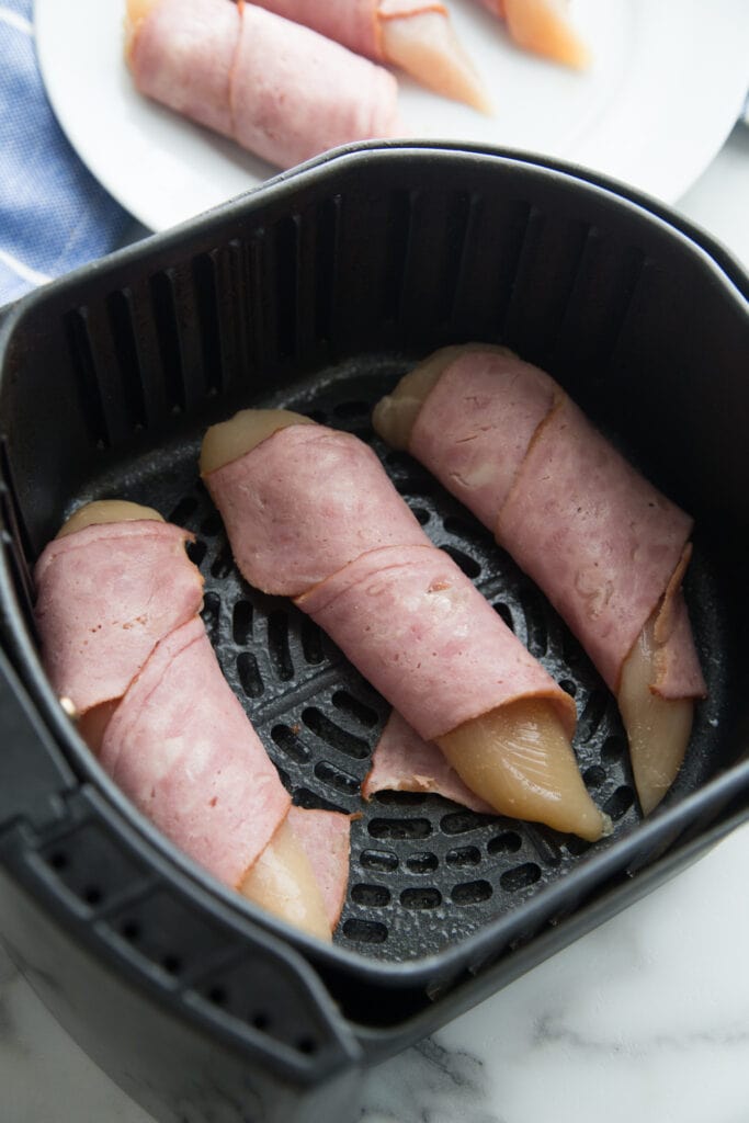 An overhead shot of an air fryer with chicken wrapped in bacon