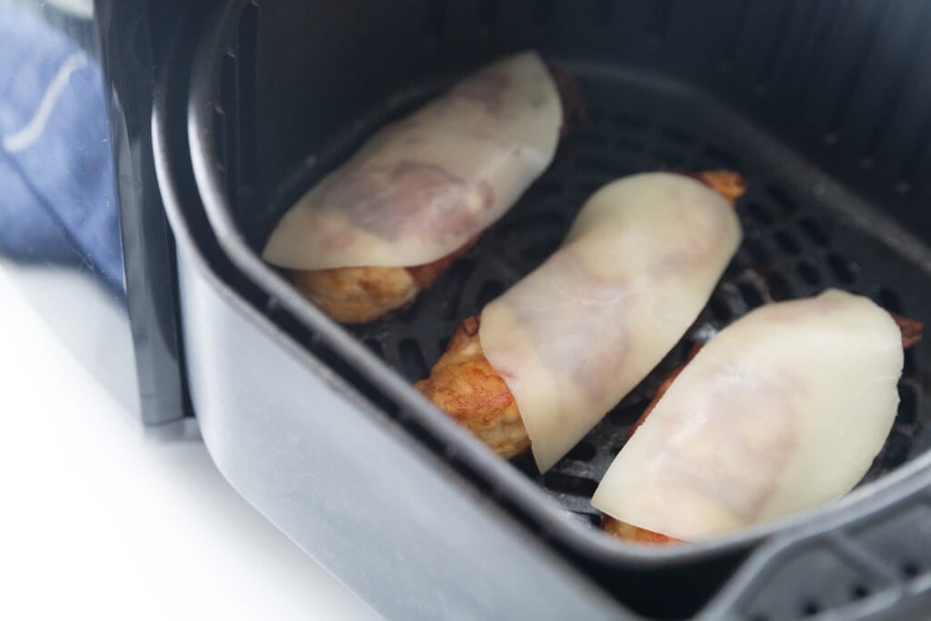 Bacon wrapped chicken tenders topped with cheese in an air fryer basket 