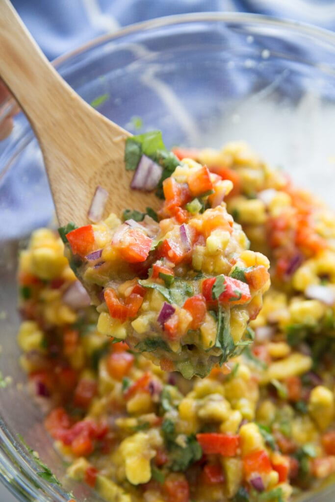 A close up of avocado peach salsa in a glass bowl on a wooden spoon. 