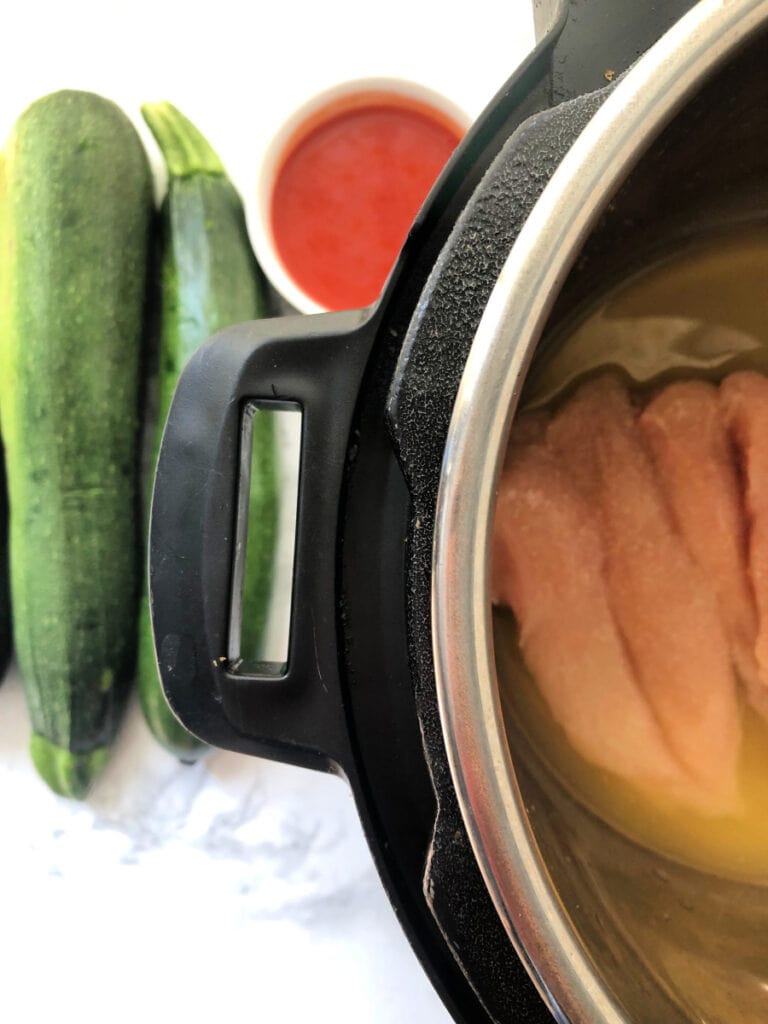 An Instant Pot with Zucchini and hot sauce nearby