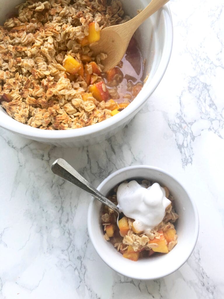 A small ramekin of Instant Pot peach crisp sitting in front of a larger bowl of Peach Crisp