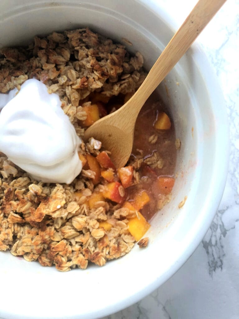 A big Instant Pot safe casserole dish with Instant Pot peach crisp topped with oats, almond flour, and so delicious coconut cream