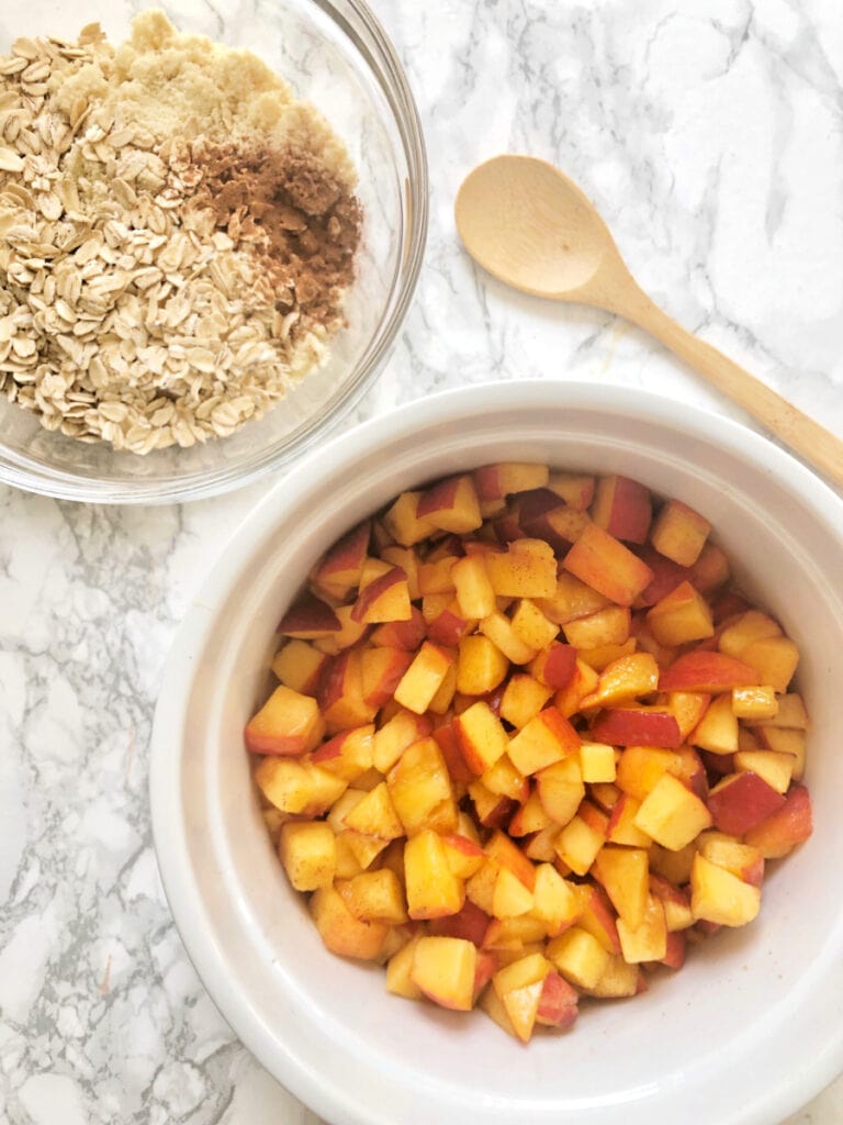 Diced peaches in a large casserole bowl sitting next to a bowl of oats, almond flour and cinnamon - this will be the topping for a Healthy Peach Crisp