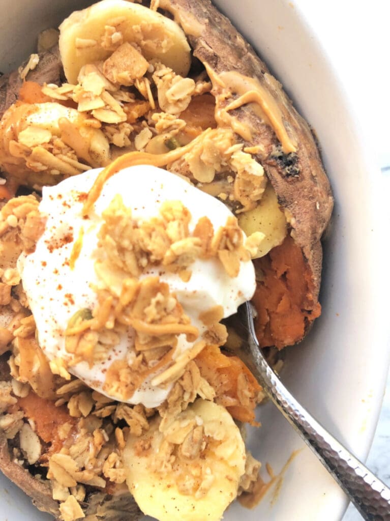 A close up of a sweet potato stuffed with bananas, granola and topped with plain Greek yogurt ready to serve as a sweet and savory snack