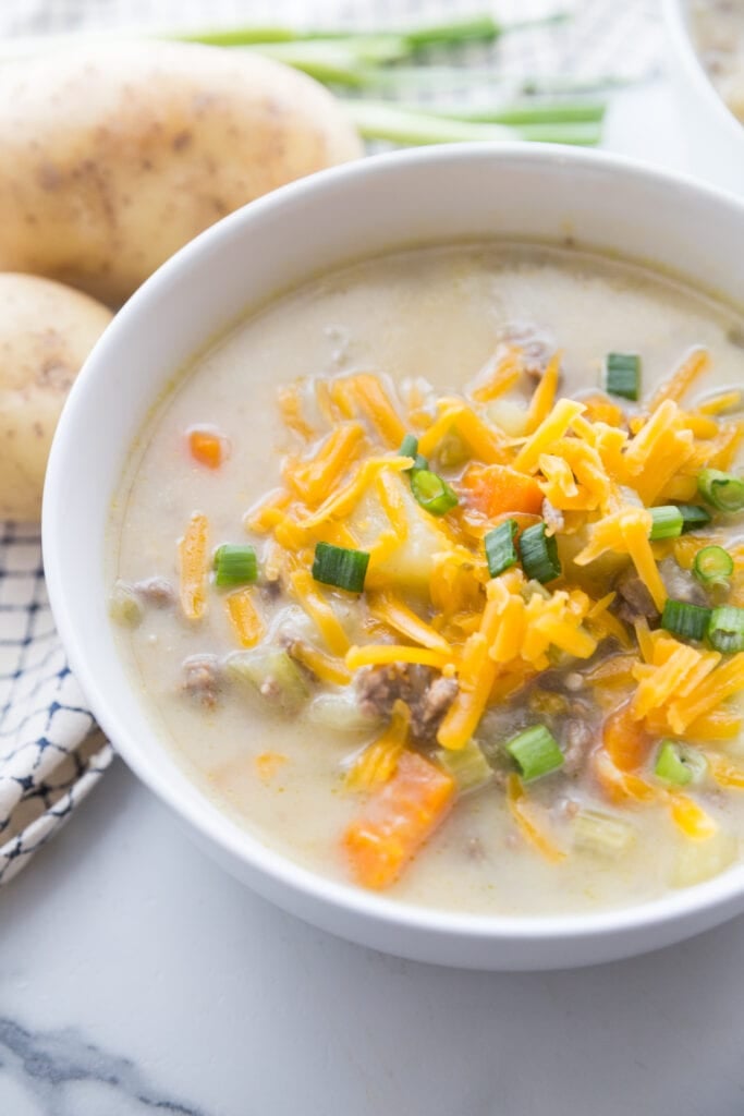 Cheeseburger soup in a white bowl, topped with shredded cheddar cheese and sliced green onions